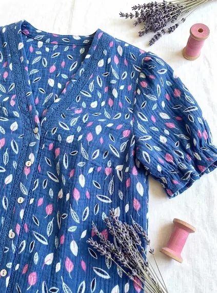 Dunkelblaue Bluse aus Musselin-Stoff mit rosa und weißen Blättern, dekoriert mit Lavendel und Garnrollen auf hellem Untergrund.