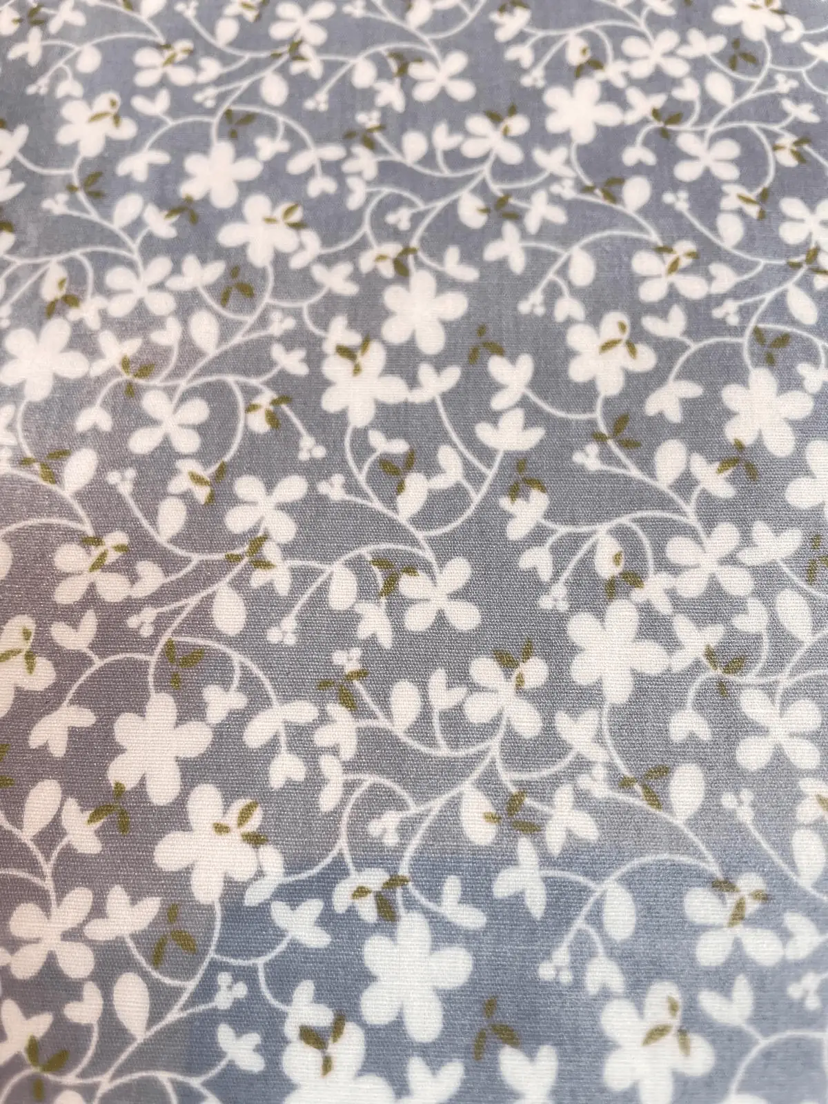 Beschichteter Baumwollstoff in Grau mit filigranen weißen Blumenranken und dezenten olivgrünen Blättern.