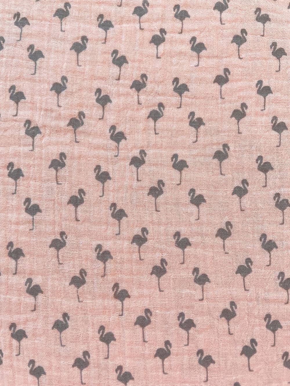 Nahaufnahme von rosa Musselin-Gewebe aus Baumwolle, bedruckt mit kleinen, grauen Flamingo-Silhouetten.