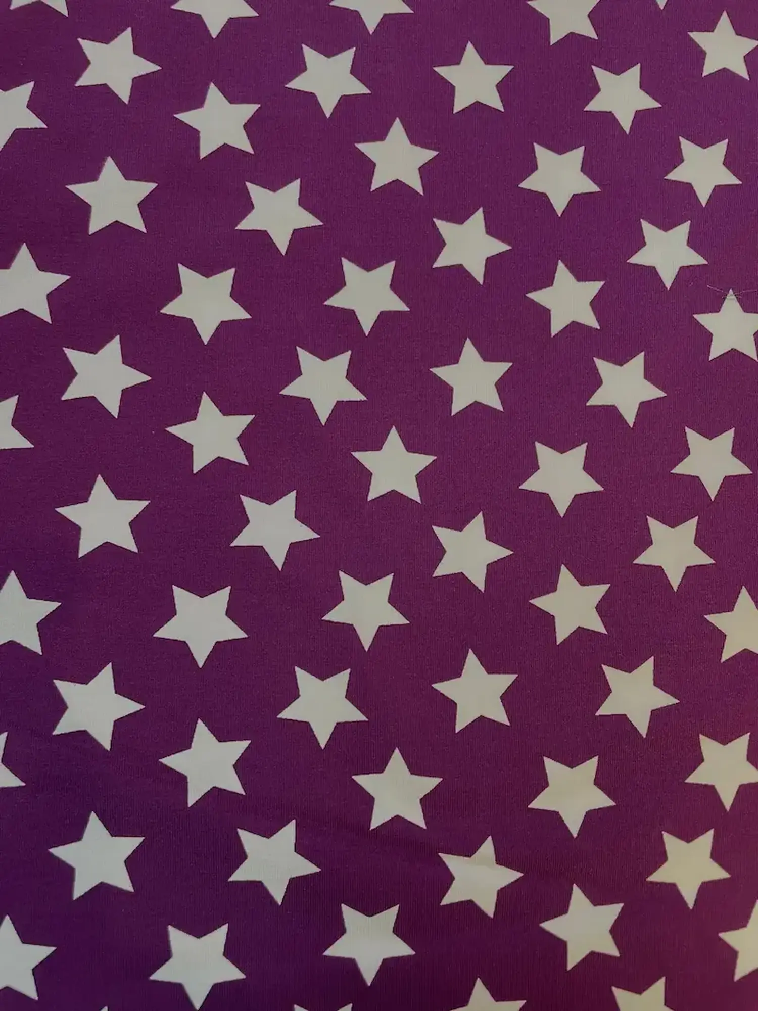 Nahaufnahme eines violetten Jerseystoffs mit einem regelmäßigen Muster aus mittelgroßen weißen Sternen, ideal als elastische Meterware für Bekleidung.