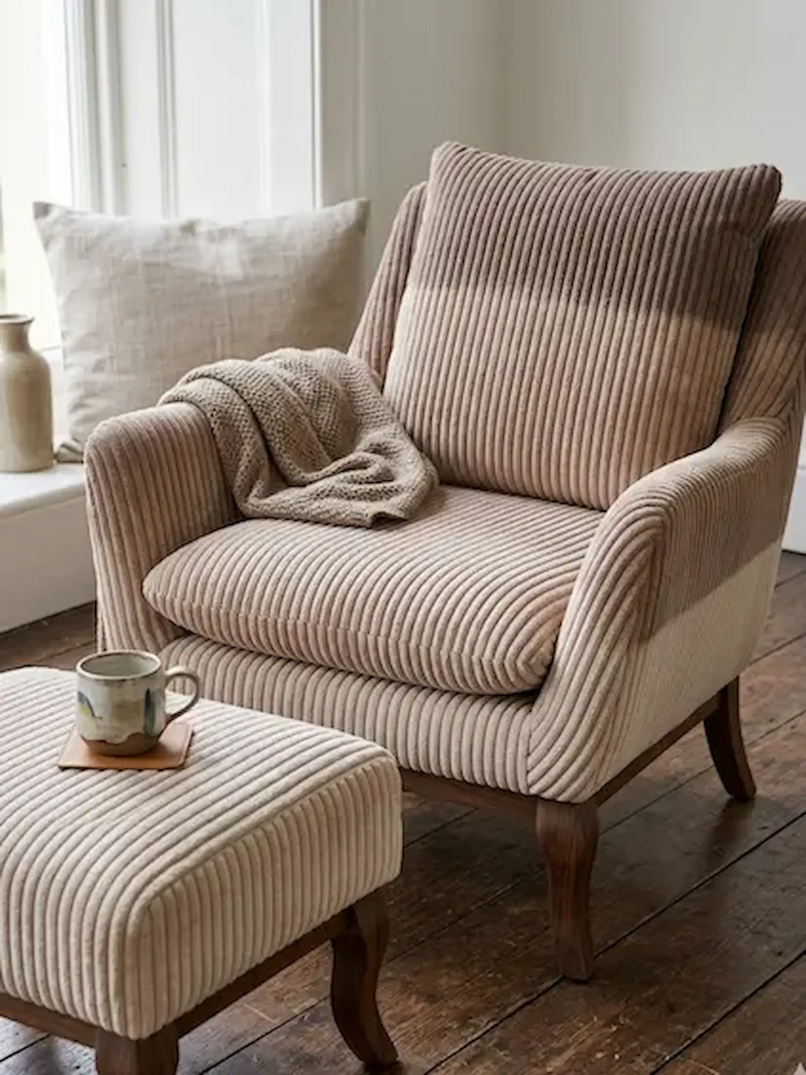 Moderner Sessel und Hocker mit Polsterbezug aus beigem Breitcord-Stoff in einem hellen Wohnzimmer.