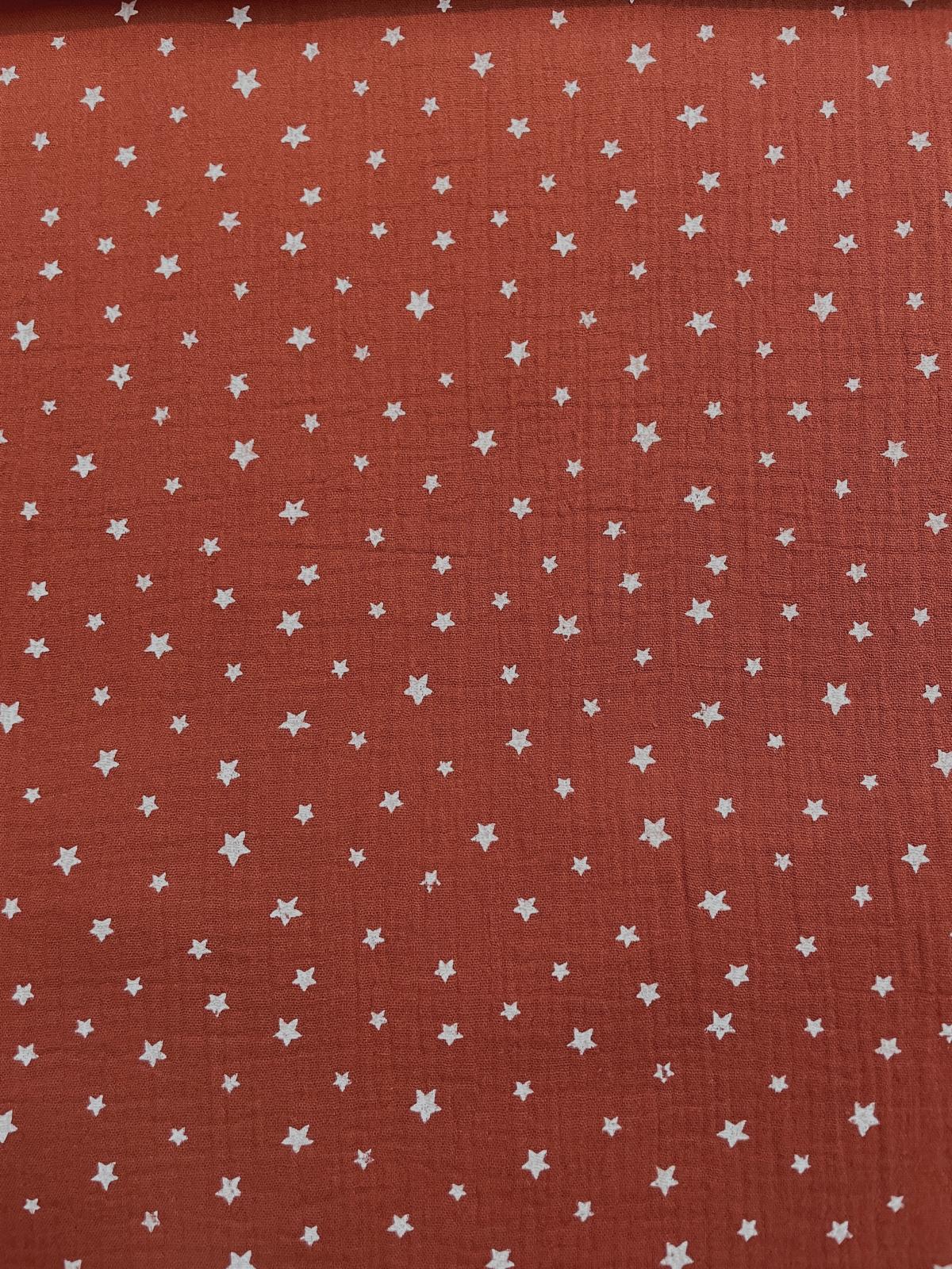 Nahaufnahme von weichem, terracottafarbenem Musselin-Stoff aus 100% Baumwolle mit kleinen weißen Sternen.