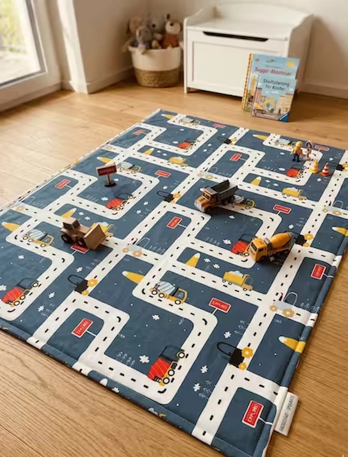 Robuster Baumwoll-Popeline-Stoff als Meterware in Dunkelblau mit Straßenverlauf und Baustellenfahrzeugen, genäht als wattierte Spielmatte auf hellem Holzfußboden.