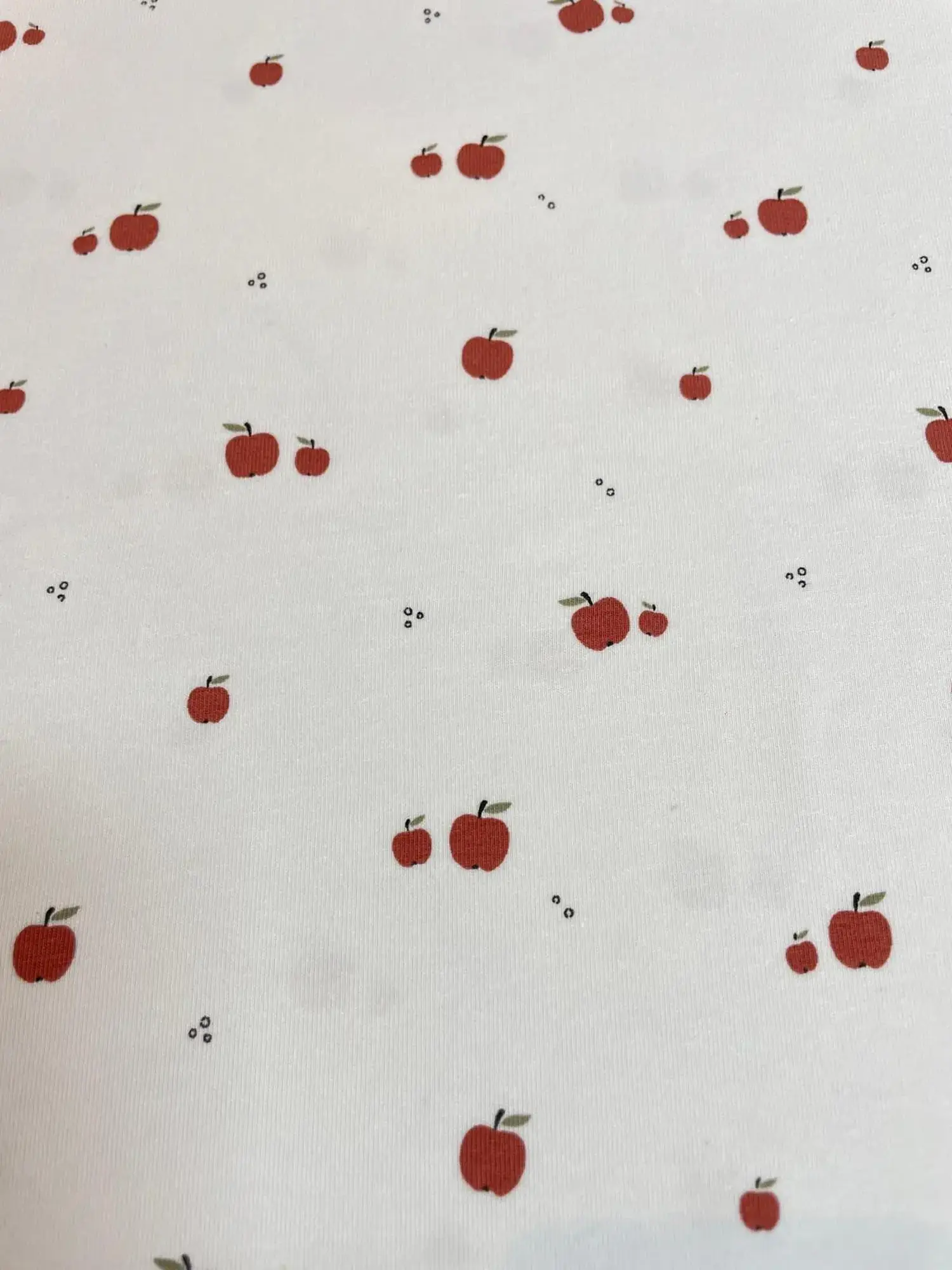 Weißer Jersey-Stoff mit kleinen roten Äpfeln und dezenten schwarzen Punkten im minimalistischen Grafik-Stil.