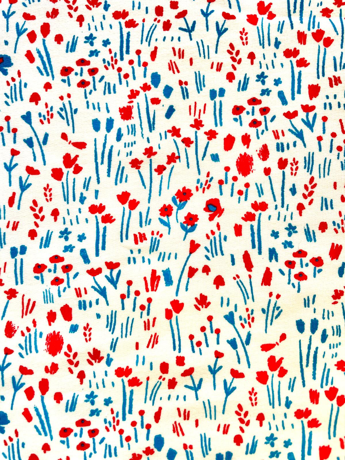 Cremeweißer Sweatstoff mit abstraktem Wildblütenmuster in Rot und BlauEine hochauflösende Nahaufnahme der Stoffstruktur. Auf einem hellen, cremeweißen Untergrund ist ein verspieltes, kleinteiliges Allover-Muster zu sehen. Die Grafik zeigt stilisierte Wild