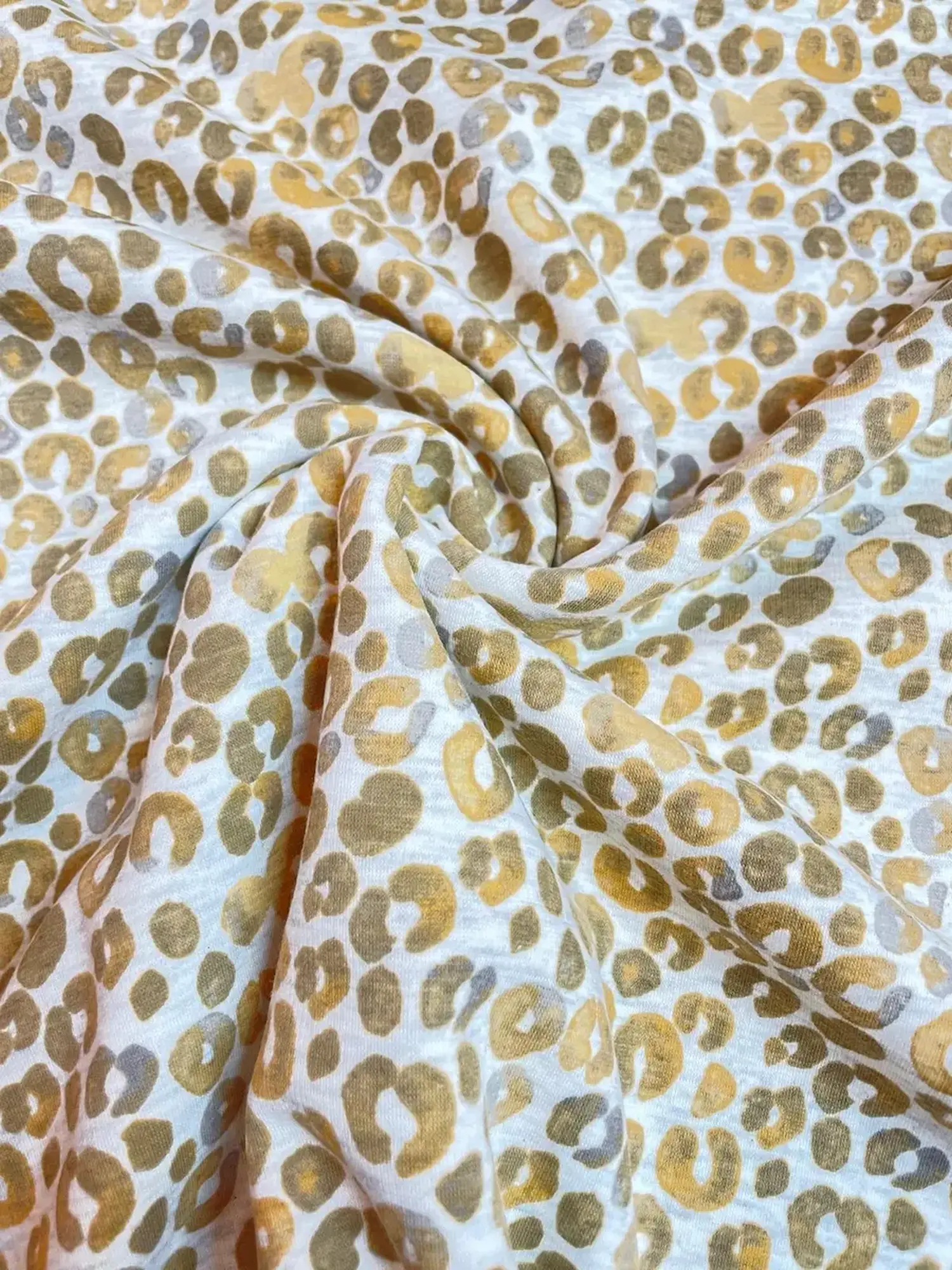 Hochwertiger Alpenfleece-Stoff mit modernem Leoparden-Print in den Farben Beige, Senfgelb und Grau. Der Stoff liegt in weichen Falten und zeigt eine feine Strickoberfläche.