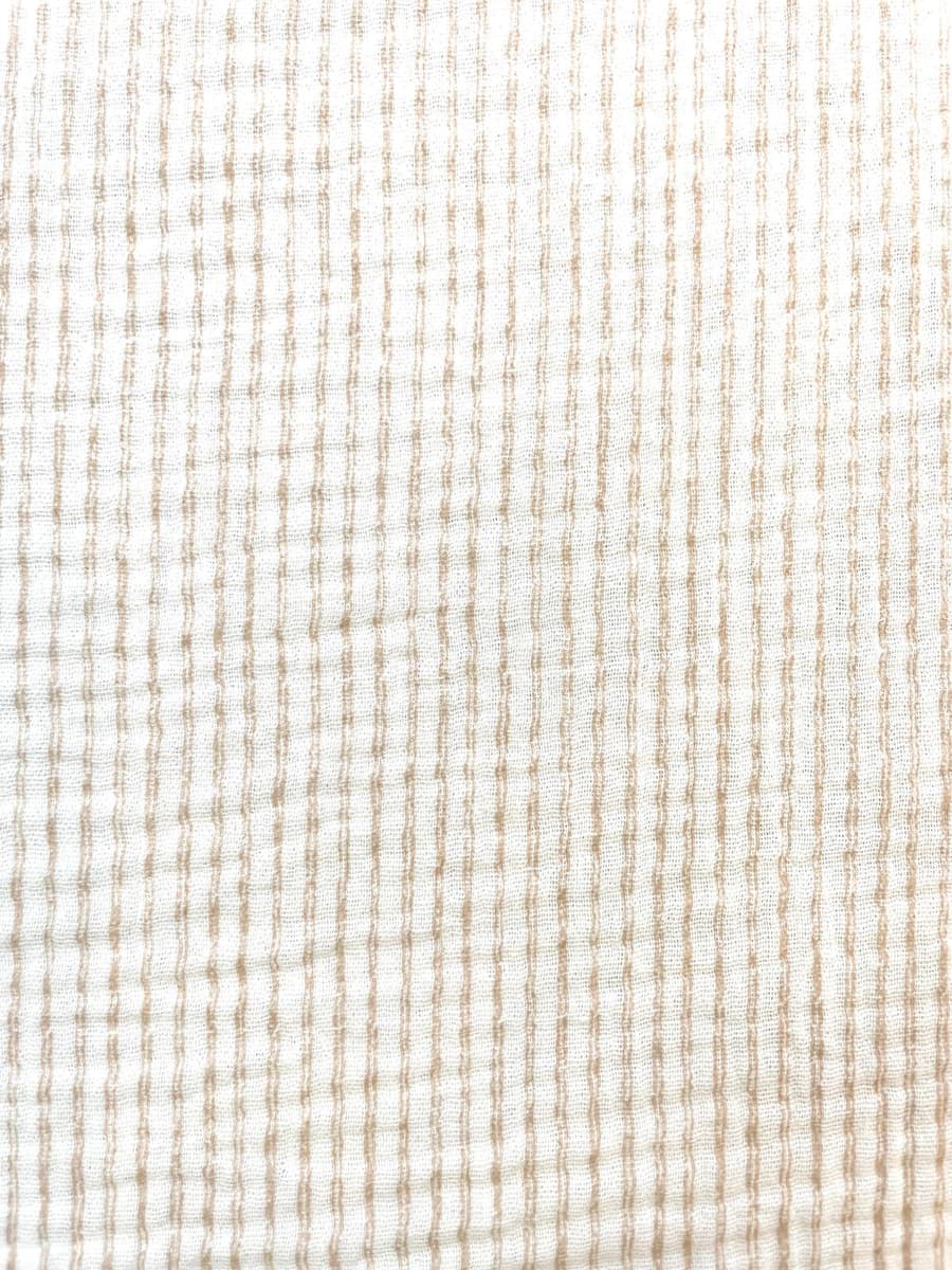 Nahaufnahme eines cremefarbenen Musselinstoffs aus 100% Baumwolle mit feinen, vertikal verlaufenden Streifen in Beige. Die charakteristische, luftige Double-Gauze-Struktur ist deutlich erkennbar.