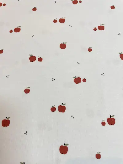Weißer Jersey-Stoff mit kleinen roten Äpfeln und dezenten schwarzen Punkten im minimalistischen Grafik-Stil.