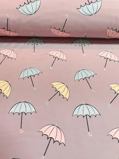 Outdoor-Softshell-Stoff in Altrosa, bedruckt mit filigranen Regenschirmen in Pastelltönen wie Hellblau, zartem Gelb und Rosa. Die Regenschirme haben schwarze Griffe und dezente Pünktlich-Muster. Hochwertiger Funktionsstoff für Mädchenjacken und Regenbekle
