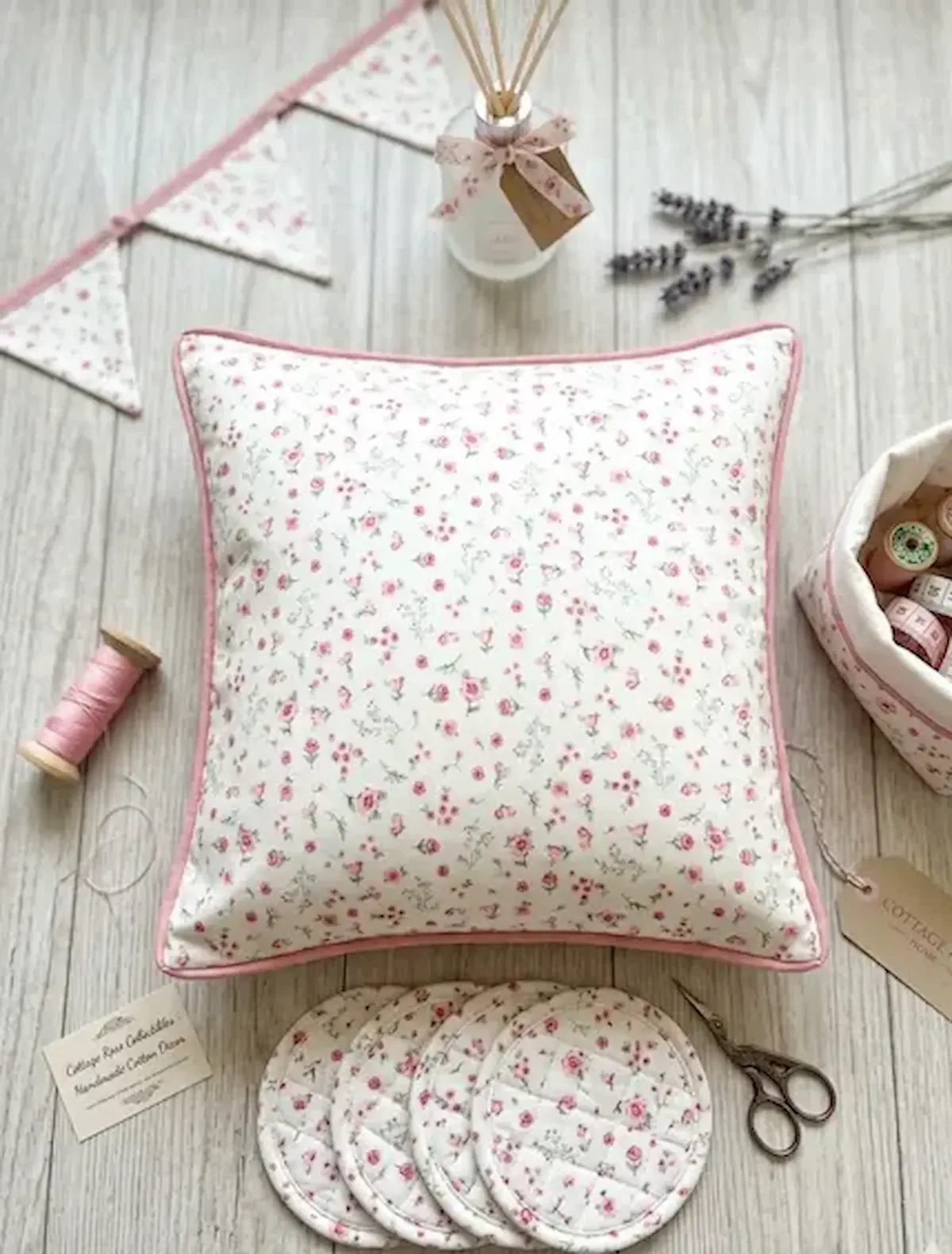Feine Baumwolle Popeline mit zartem Streublumen-Muster in Rosa und Weiß, flachliegend präsentiert als Dekokissen, Wimpelkette und Untersetzer.