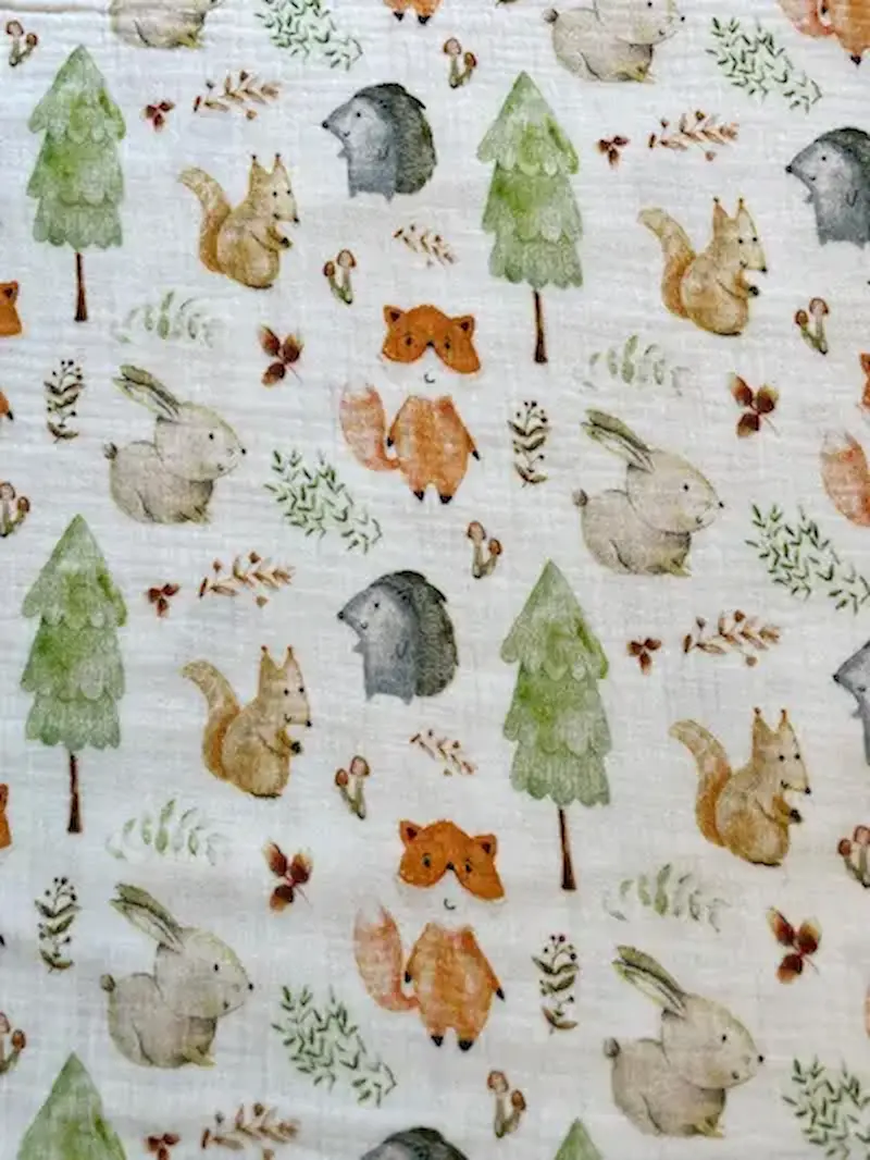 Cremefarbener Musselinstoff mit buntem Waldtiere-Print bestehend aus Fuchs, Eichhörnchen, Hase, Igel, Tannen und Pilzen. 100% Baumwolle, Double-Gauze Qualität.