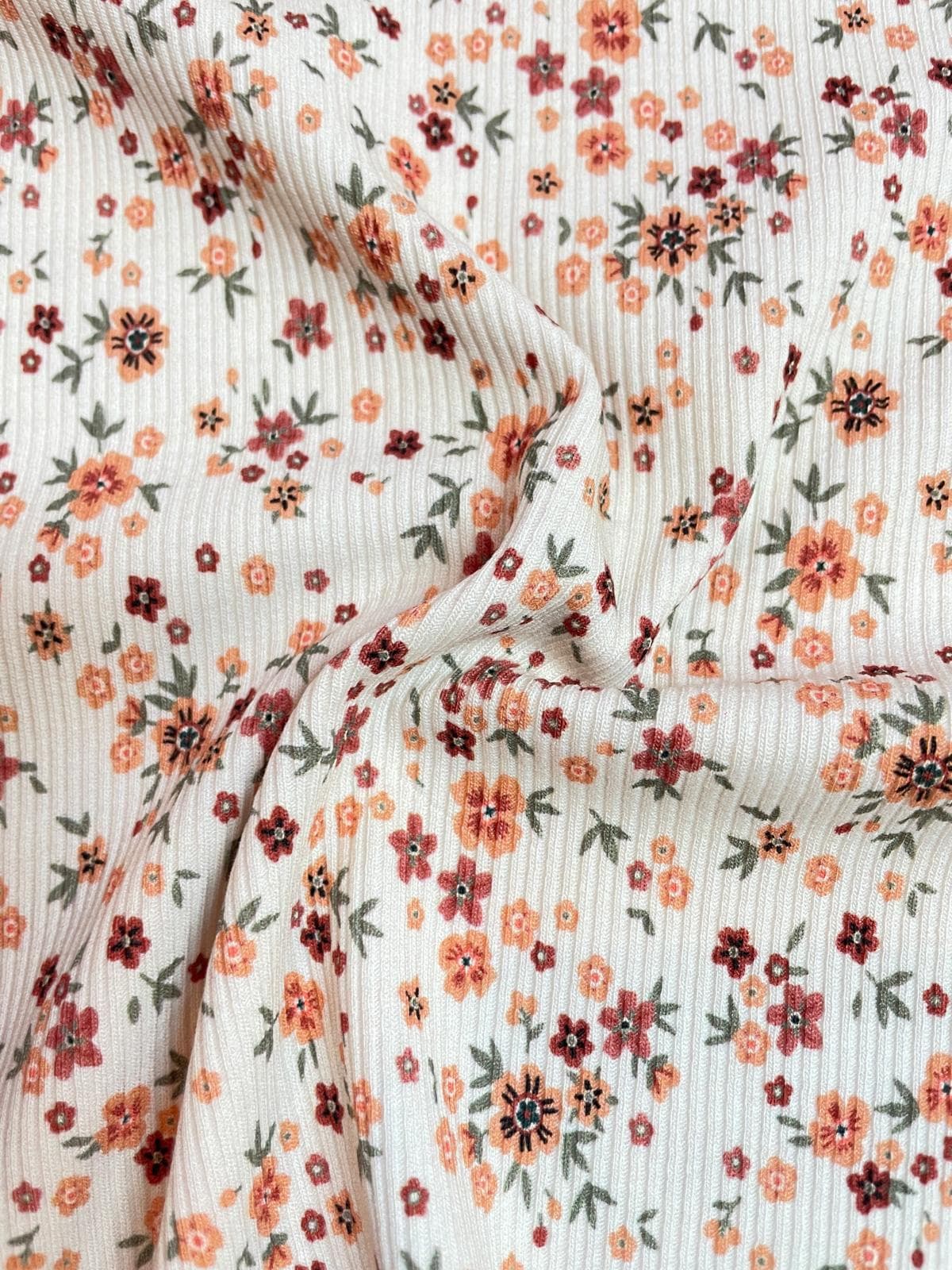 Weicher Rippjersey Stoff mit kleinem Streublumen-Muster in Orange und Rost auf hellem Grund, elastischer Rippstrick für Baby- und Kinderkleidung, Meterware.