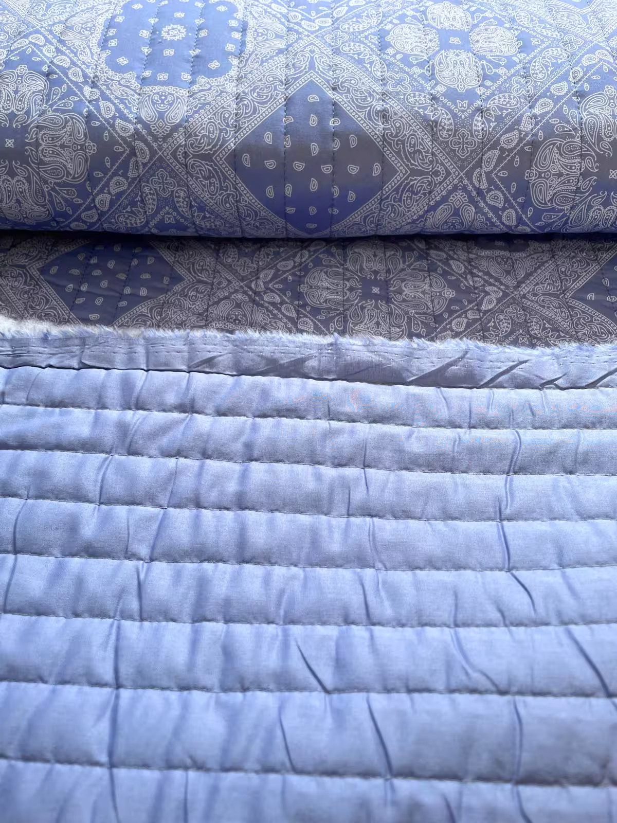 Nahaufnahme eines wendbaren Steppstoffs als Meterware: Eine Seite mit blauem Paisley-Muster, die andere Seite in schlichtem Blau, ideal für vielseitige Nähprojekte