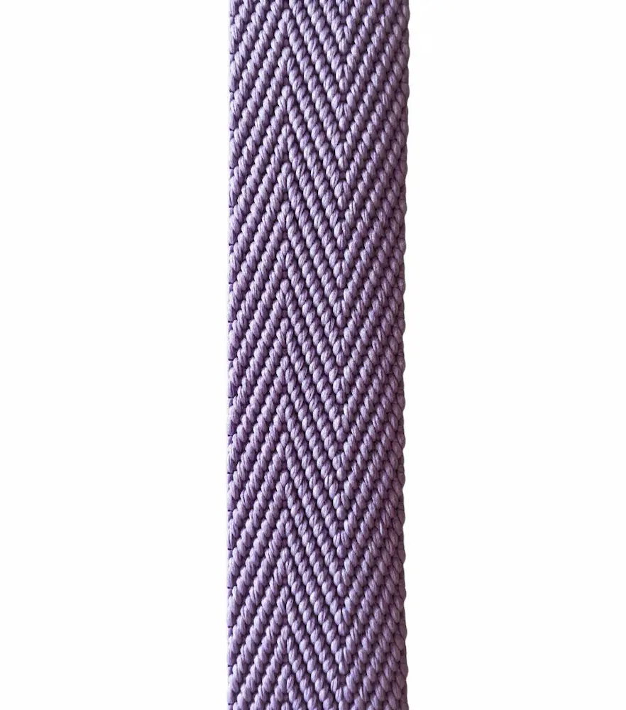Nahaufnahme von einem fliederfarbenen Gurtband mit 3 cm Breite und elegantem Fischgrat-Muster vor weißem Hintergrund, Meterware für Taschenriemen.