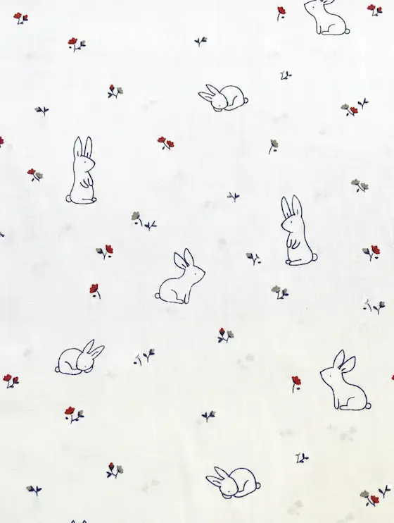 Hochwertiger weißer Stoff mit feinem Print aus minimalistisch gezeichneten Hasen und kleinen roten Blüten – perfekt für Oster-Nähprojekte und Frühlings-Deko von Stoffpfau.