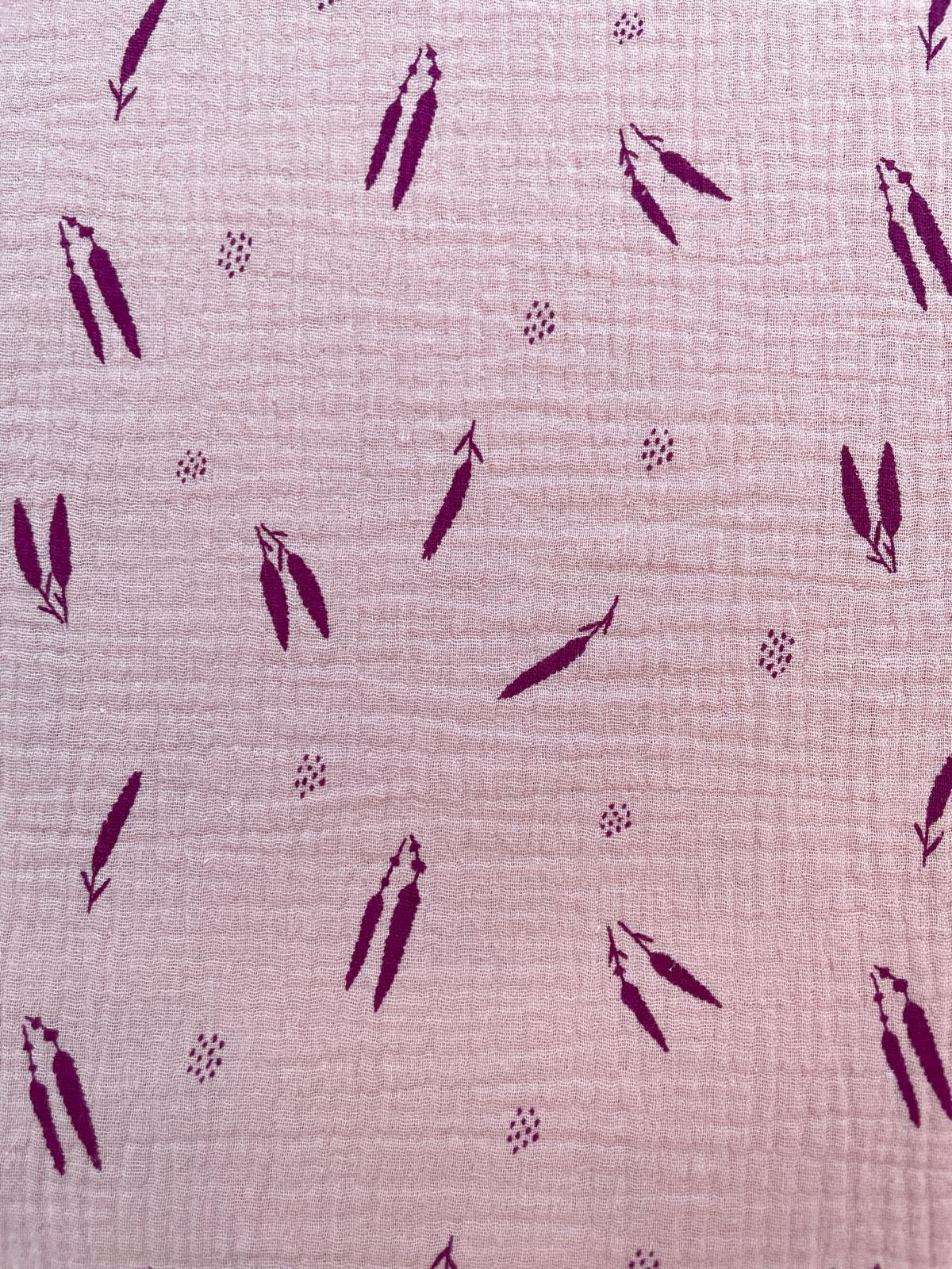 Nahaufnahme eines altrosafarbenen Musselinstoffs mit einem Muster aus dunkelbeerfarbenen Federn und kleinen Pünktchen-Akzenten. Die weiche Double-Gauze-Struktur aus reiner Baumwolle ist deutlich erkennbar.