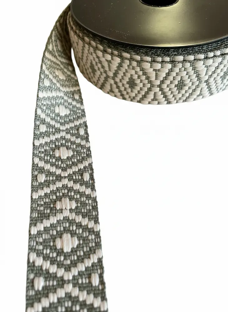 Gewebtes Gurtband mit 38mm Breite im Ethno-Stil auf einer schwarzen Rolle, geometrisches Rautenmuster in Salbeigrün und Creme als Meterware für Taschenriemen