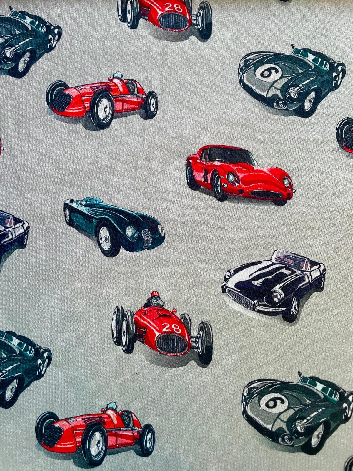 Klassischer Sweatstoff in Grau mit einem Allover-Print aus roten, grünen und schwarzen Retro-Rennwagen, ideal als Meterware für Kleidung.