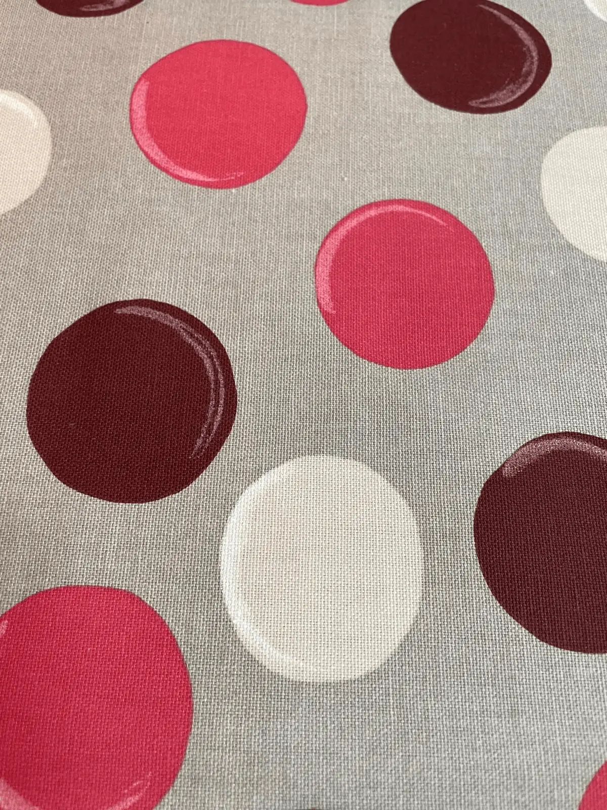 Nahaufnahme von beschichteter Baumwolle mit großen Punkten in Beerenrot, Weinrot und Creme auf grauem Hintergrund