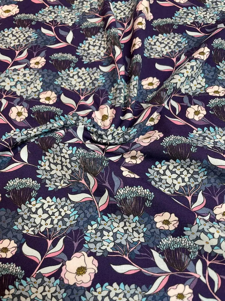 Hochwertiger Jersey-Stoff mit filigranem floralem Muster. Zu sehen sind hellblaue Hortensien und kleine rosa Blüten auf einem tiefdunkelblauen Hintergrund. Ideal für Kleider und Shirts.