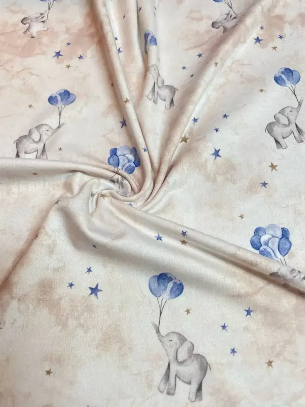 Cremefarbener Jersey-Stoff mit Aquarell-Optik, kleinen grauen Elefanten, die blaue Luftballons halten, und blauen sowie goldenen Sternen.