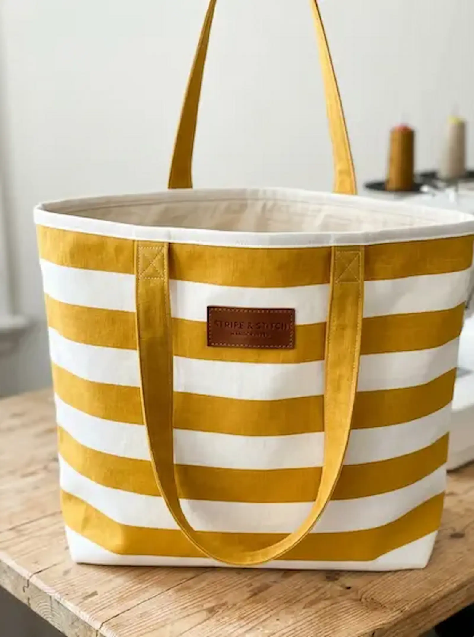 Große Shopper-Tasche aus gelb-weiß gestreiftem Baumwoll-Popeline Stoff mit stabilen Henkeln auf einem Holztisch.