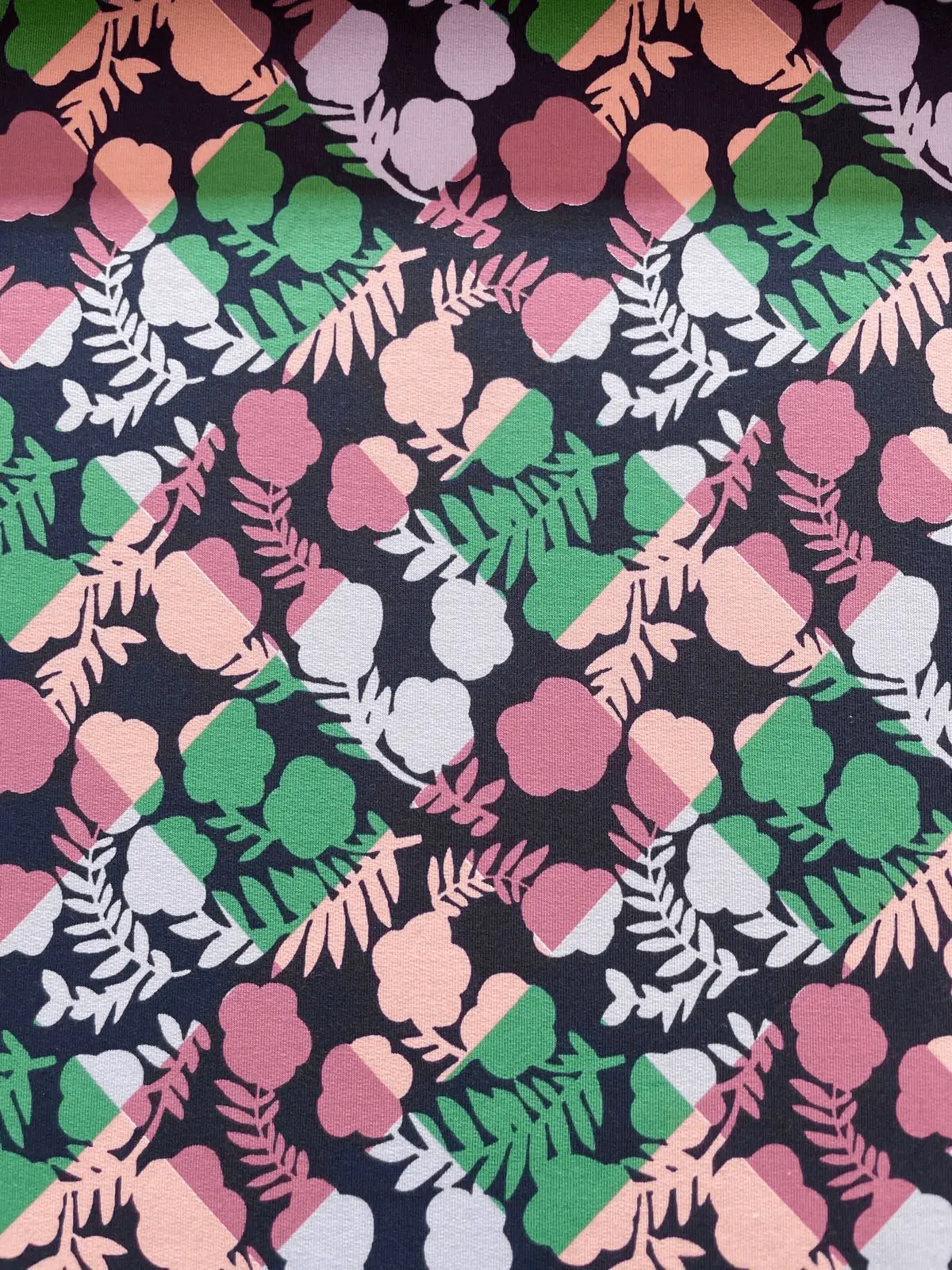 Detailansicht eines French Terry Stoffes als Meterware mit einem modernen, grafischen Blumen- und Blattmuster in bunten Farben auf dunkelblauem Untergrund, perfekt für Hoodies und Sweatshirts.