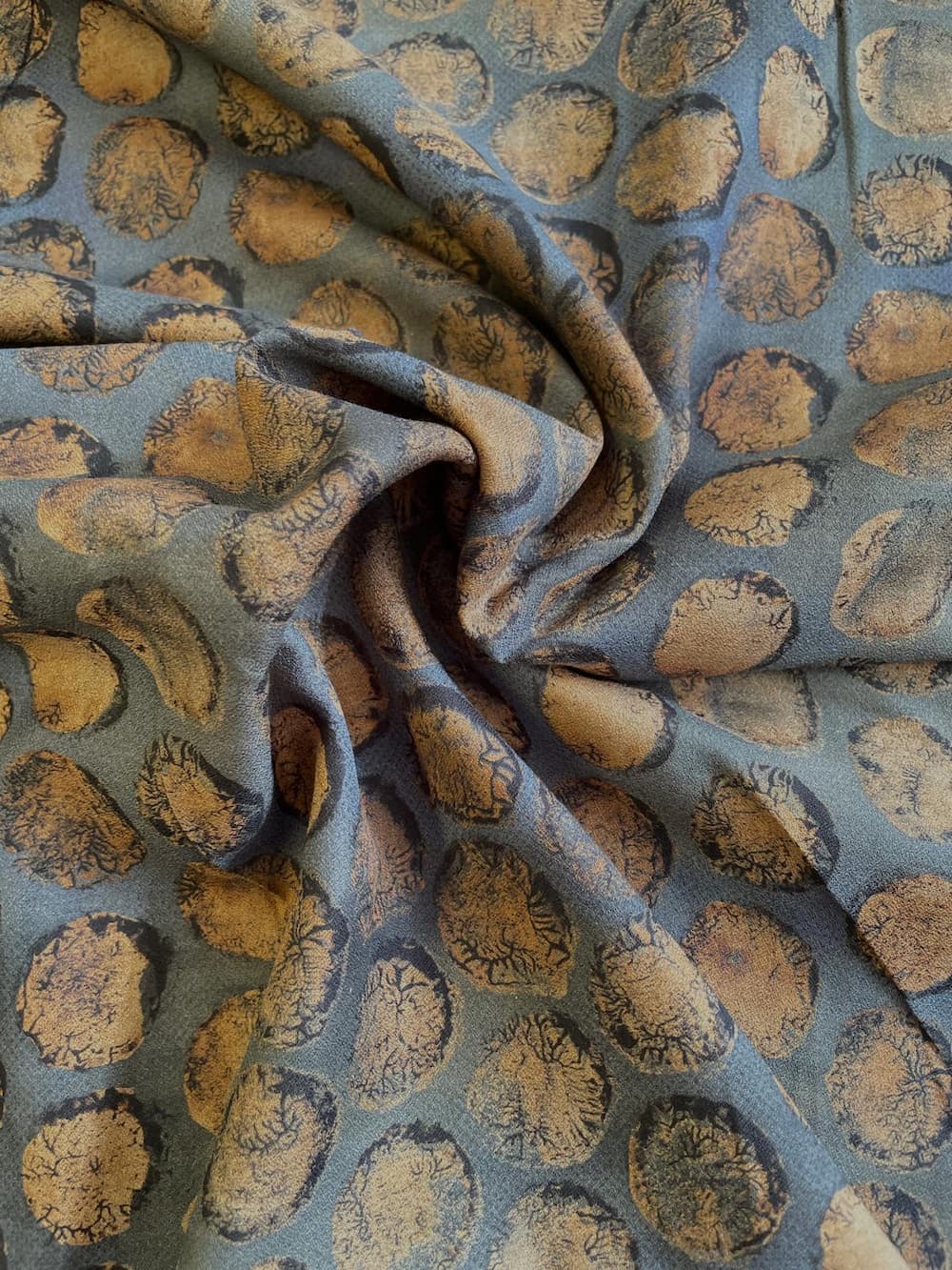 Drapierter und in Falten gelegter Baumwoll-Krepp-Stoff als Meterware mit strukturierter Oberfläche und Kreis-Muster in Blau und Bronze