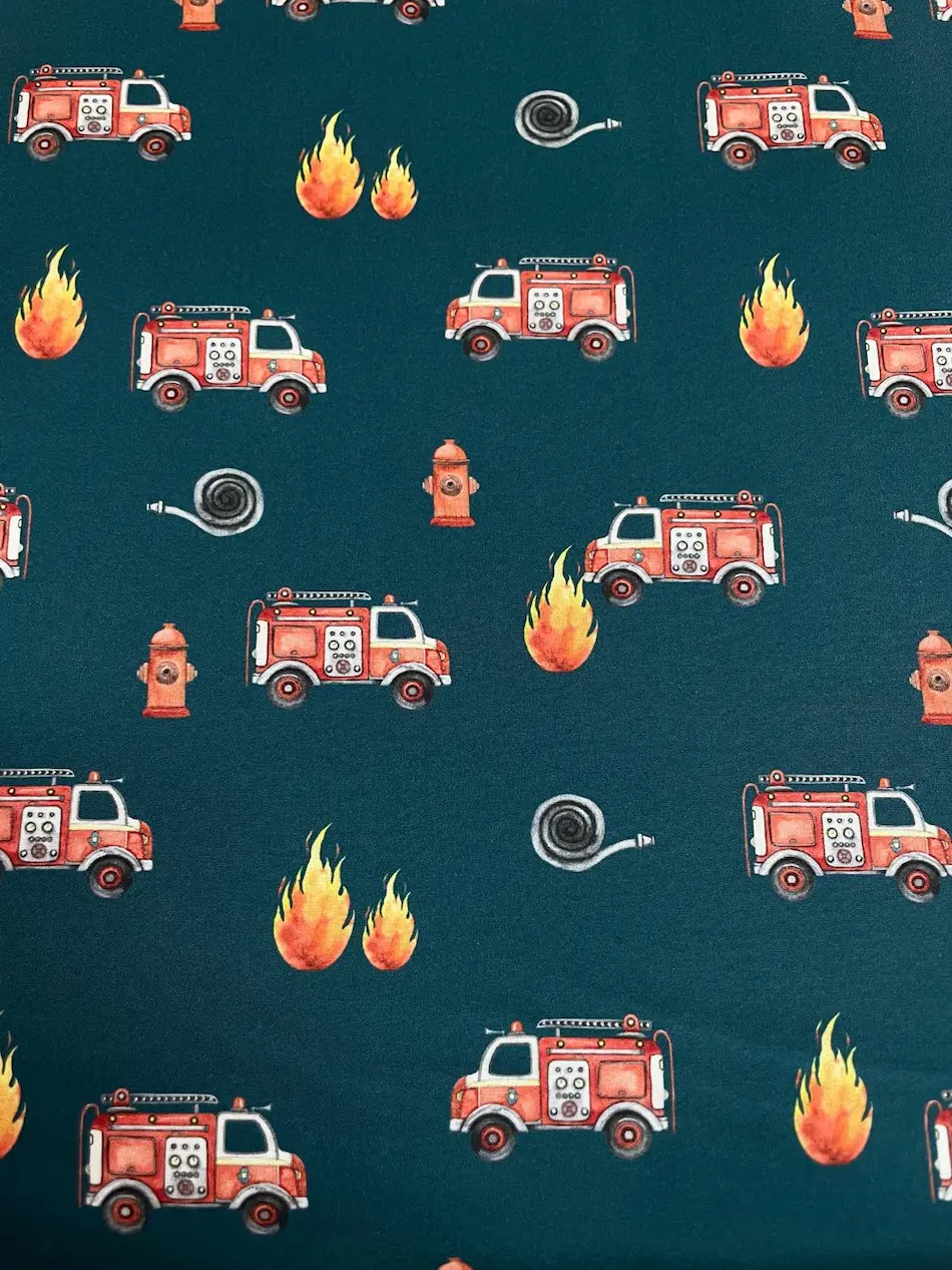 Wasserabweisender Softshell-Stoff mit Feuerwehrmotiven auf dunkelpetrolfarbenem Hintergrund. Das Muster zeigt rote Feuerwehrautos, lodernde Flammen, Hydranten und aufgerollte Feuerwehrschläuche. Ein detailreicher Outdoorstoff für mutige kleine Alltagsheld