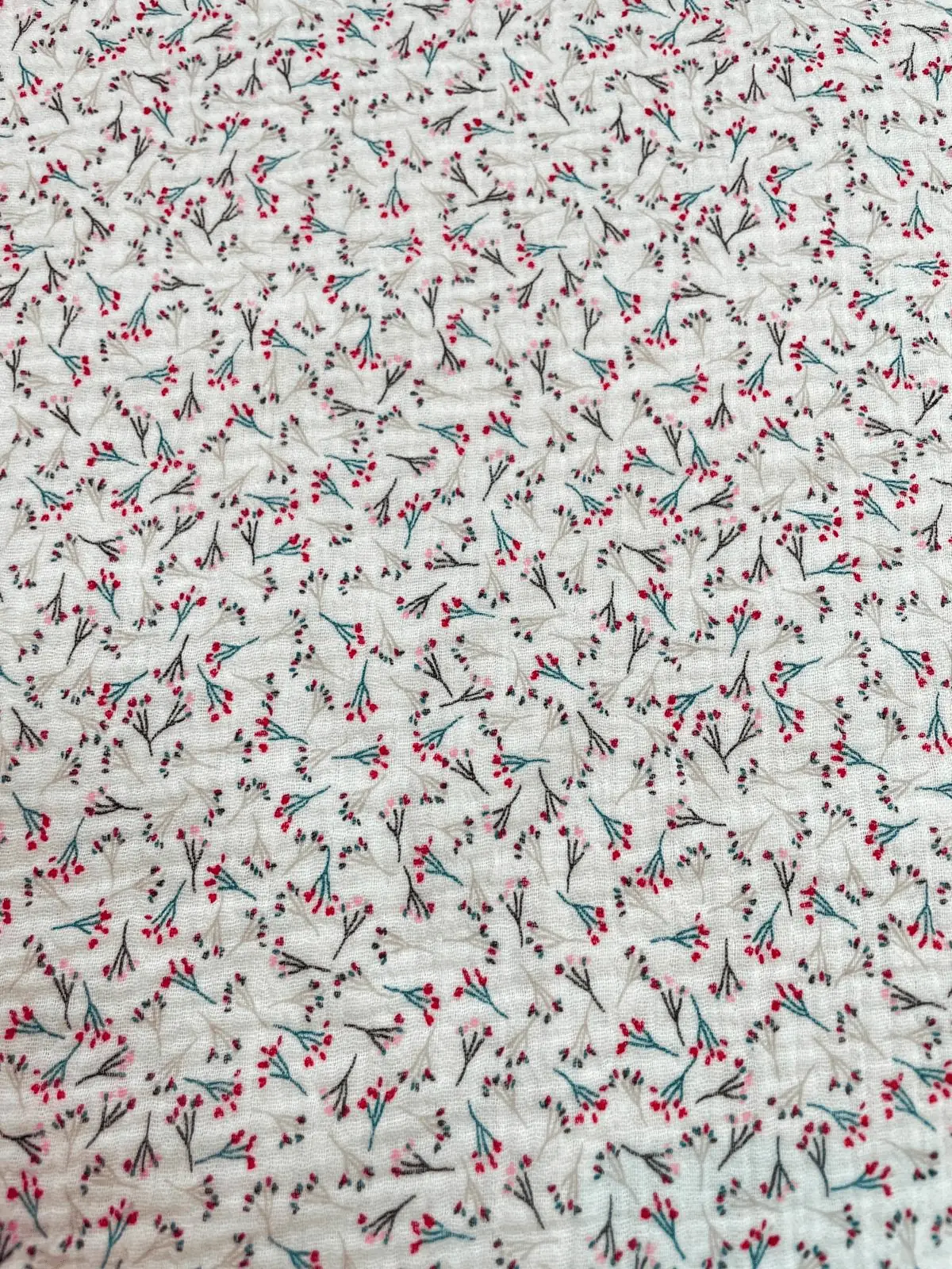 Weißer Musselin-Stoff mit feinem Muster aus roten und blauen Beeren-Zweigen. Hochwertige Double-Gauze Baumwoll-Meterware mit charakteristischer Crinkle-Optik.
