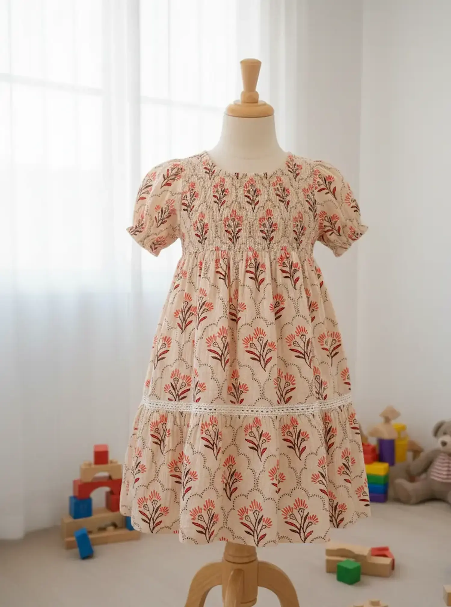 Musselin-Meterware im Boho-Stil in Beige mit herbstlichem Blumenmuster in Rot und Braun. Das Designbeispiel zeigt ein gerafftes Mädchenkleid auf einer Holz-Schneiderpuppe vor hellem Hintergrund. Ideal für romantische Nähprojekte.