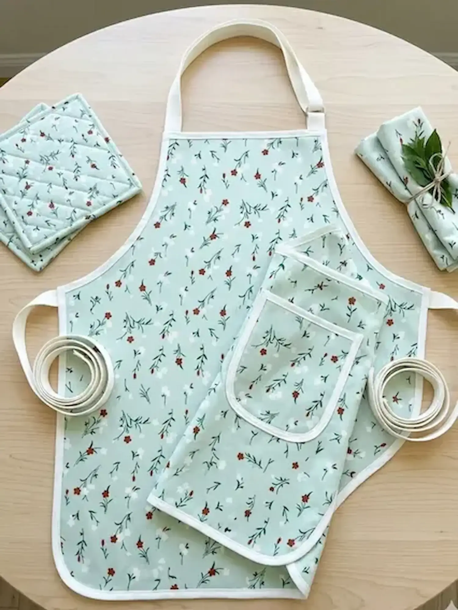 Küchenset aus mintfarbener Kochbaumwolle mit filigranem Blumenmuster, bestehend aus Schürze, Topflappen und Servietten.