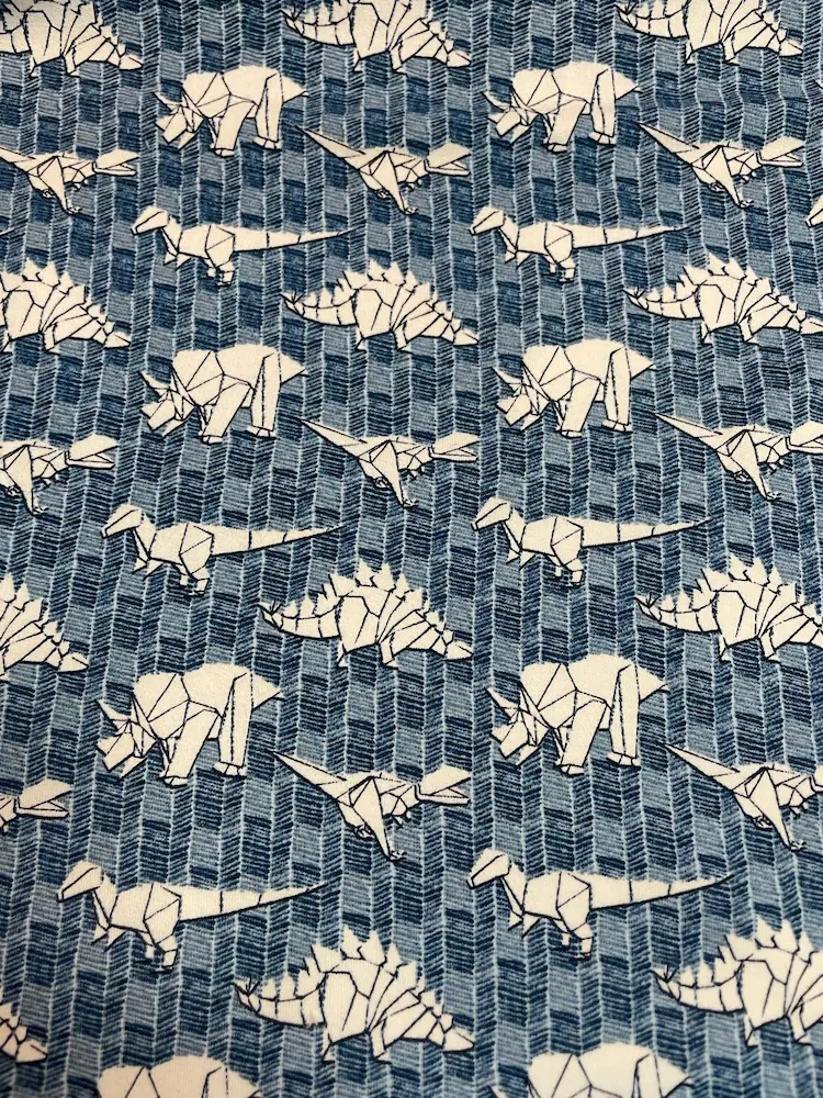 Angerauter Sweat Stoff mit Origami-Dinosaurier-Motiven in Weiß auf blauem Mustergrund, weicher Kuschelsweat für Kinderkleidung.