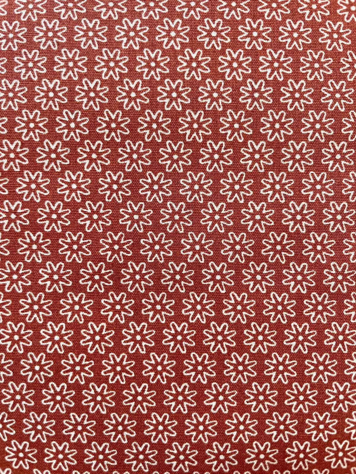 Hochwertige Baumwolle Webware Meterware in Rostbraun-Terrakotta mit einem gleichmäßigen, geometrischen Allover-Muster aus kleinen, weißen Retro-Blüten.