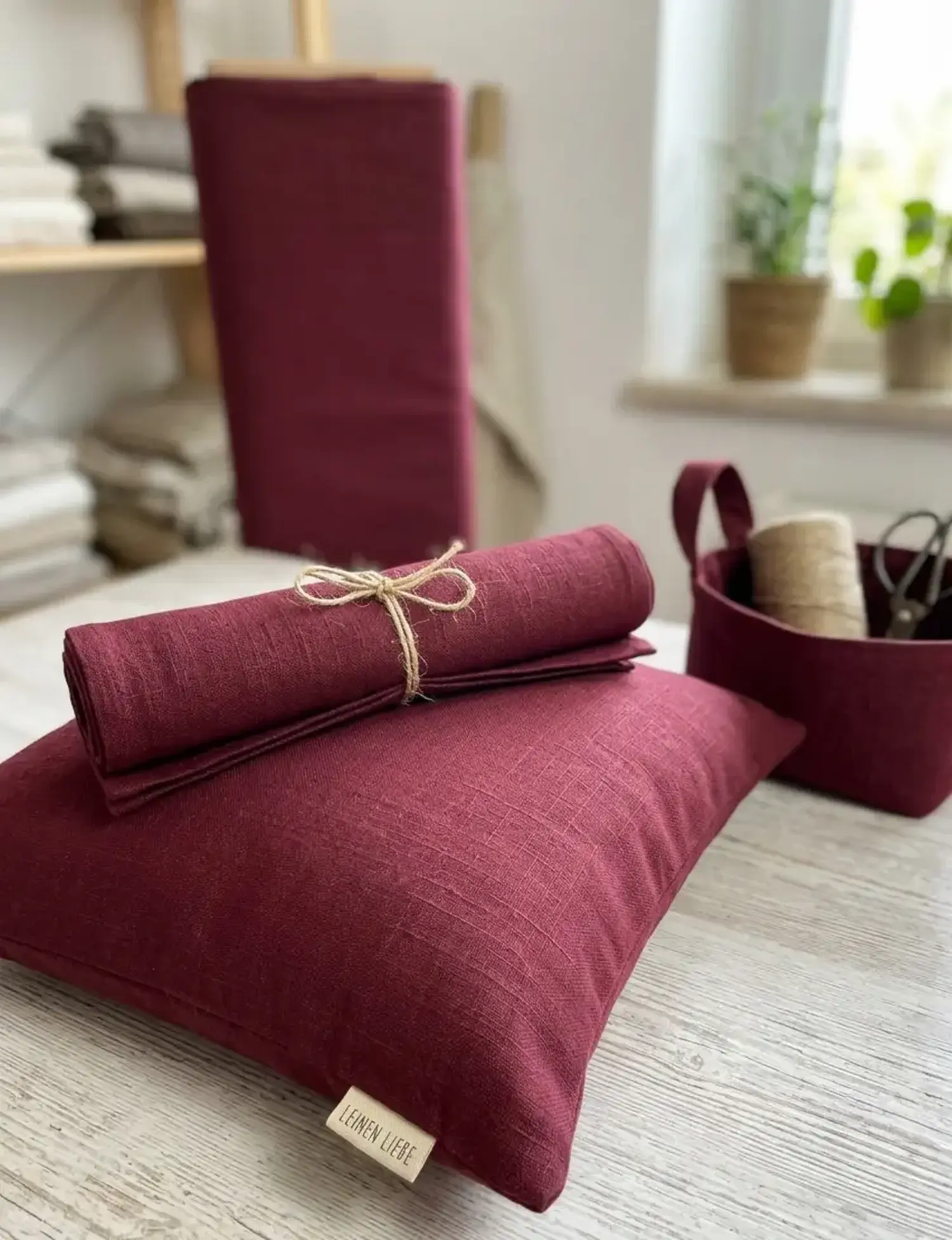 Ramie Leinen Stoff in Beerenrot als Meterware, verarbeitet zu einem Dekokissen mit 'Leinen Liebe' Label und Stoffserviette auf hellem Holztisch.