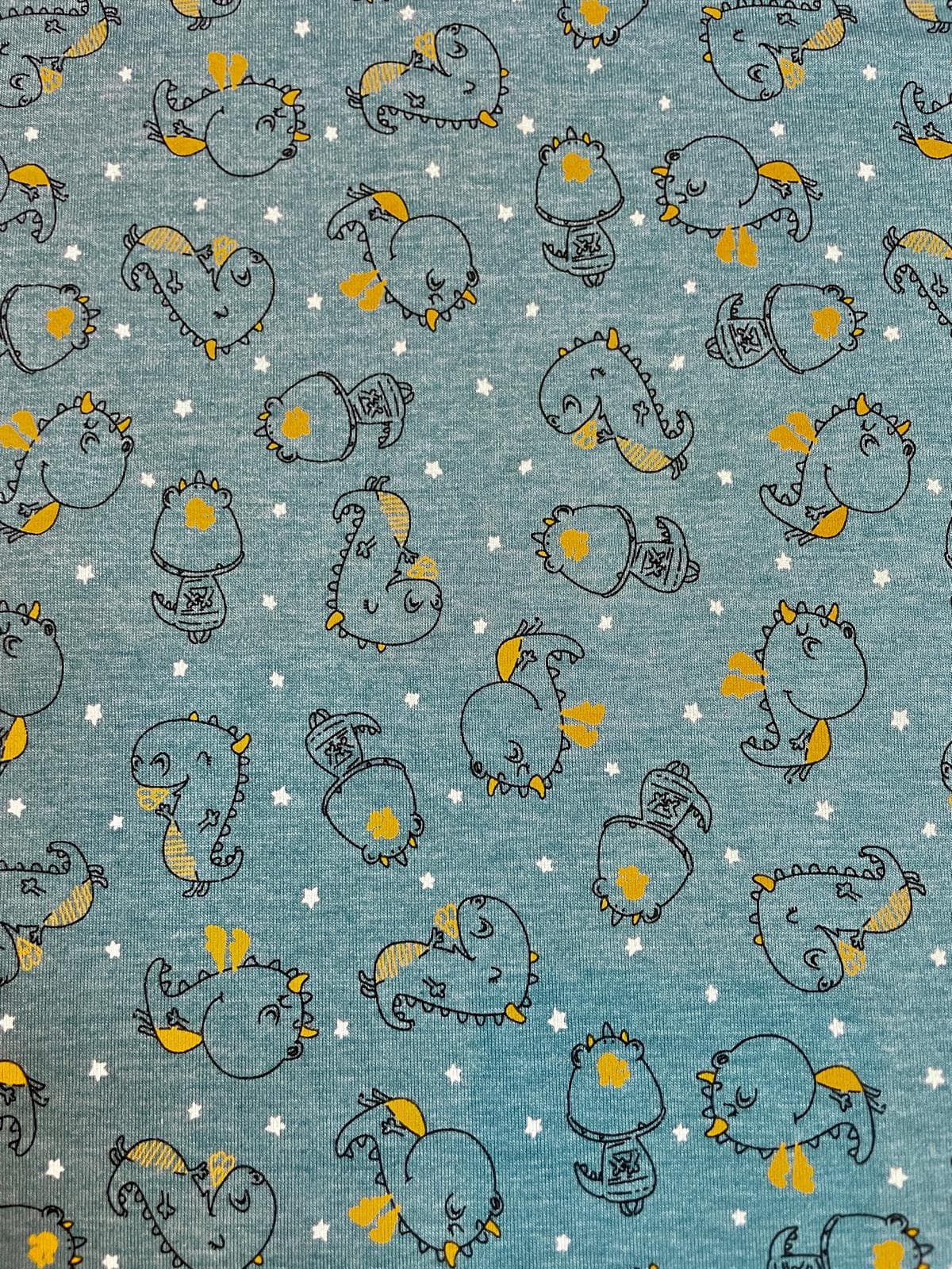 Ein flach liegender Baumwolljersey-Stoff als Meterware in Blau-Melange, bedruckt mit einem dichten Kindermuster aus skizzierten Dinosauriern und kleinen Drachen mit ocker-goldenen Akzenten, umgeben von kleinen weißen Sternen.