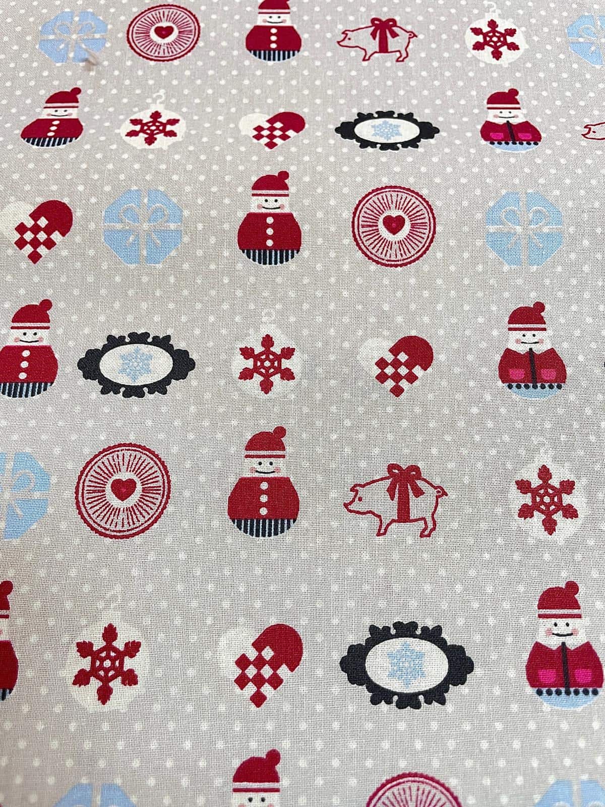Verspielter Baumwollstoff als Meterware mit kleinen Schneemännern, Geschenken, Glücksschweinchen und Schneeflocken auf hellgrauem Hintergrund mit weißen Punkten.