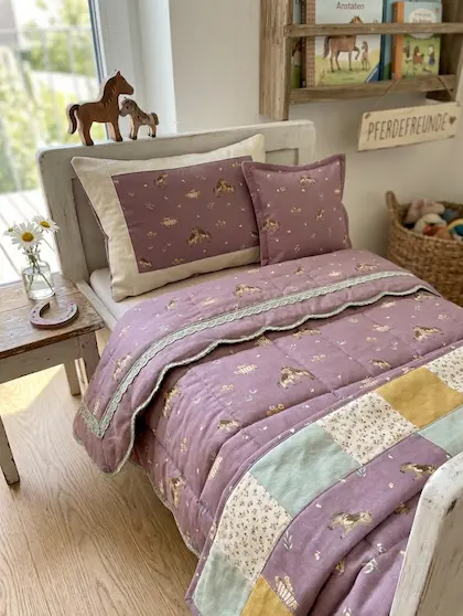 Gemütliches Kinderbett mit handgenähter Patchwork-Bettwäsche und Kissen aus mauvefarbenem Baumwollstoff mit Pferdemotiv.