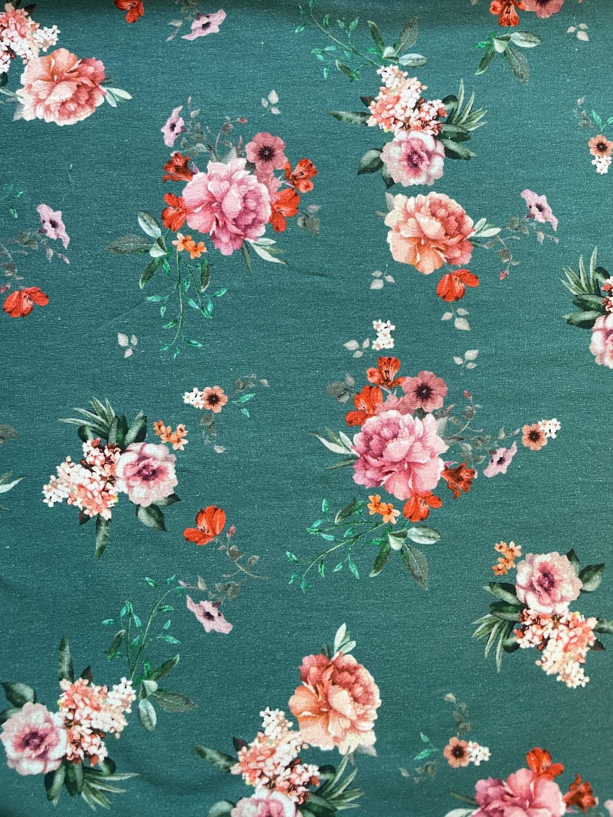 Nahaufnahme von dunkelgrünem Baumwolljersey als Meterware mit einem eleganten Allover-Print aus realistisch gezeichneten Pfingstrosen und Rosen-Bouquets in Rosa, Pfirsich und Weiß mit filigranen grünen Blättern.