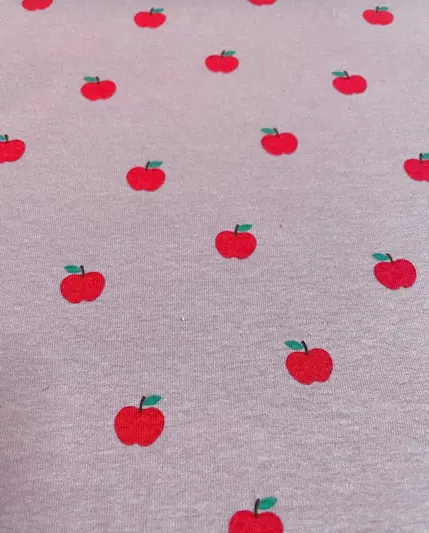 Elastischer Jersey-Stoff in meliertem Altrosa mit einem gleichmäßigen Muster aus kleinen, leuchtend roten Äpfeln mit grünen Blättern. Ideal für Kinderbekleidung und Accessoires.