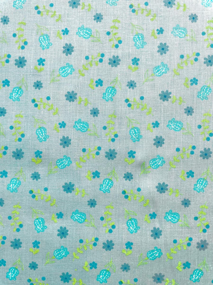 Nahaufnahme einer hellen türkis-blaugrauen Baumwoll-Webware mit einem kleinen, dezenten Blumenmuster in Grün und Blau.