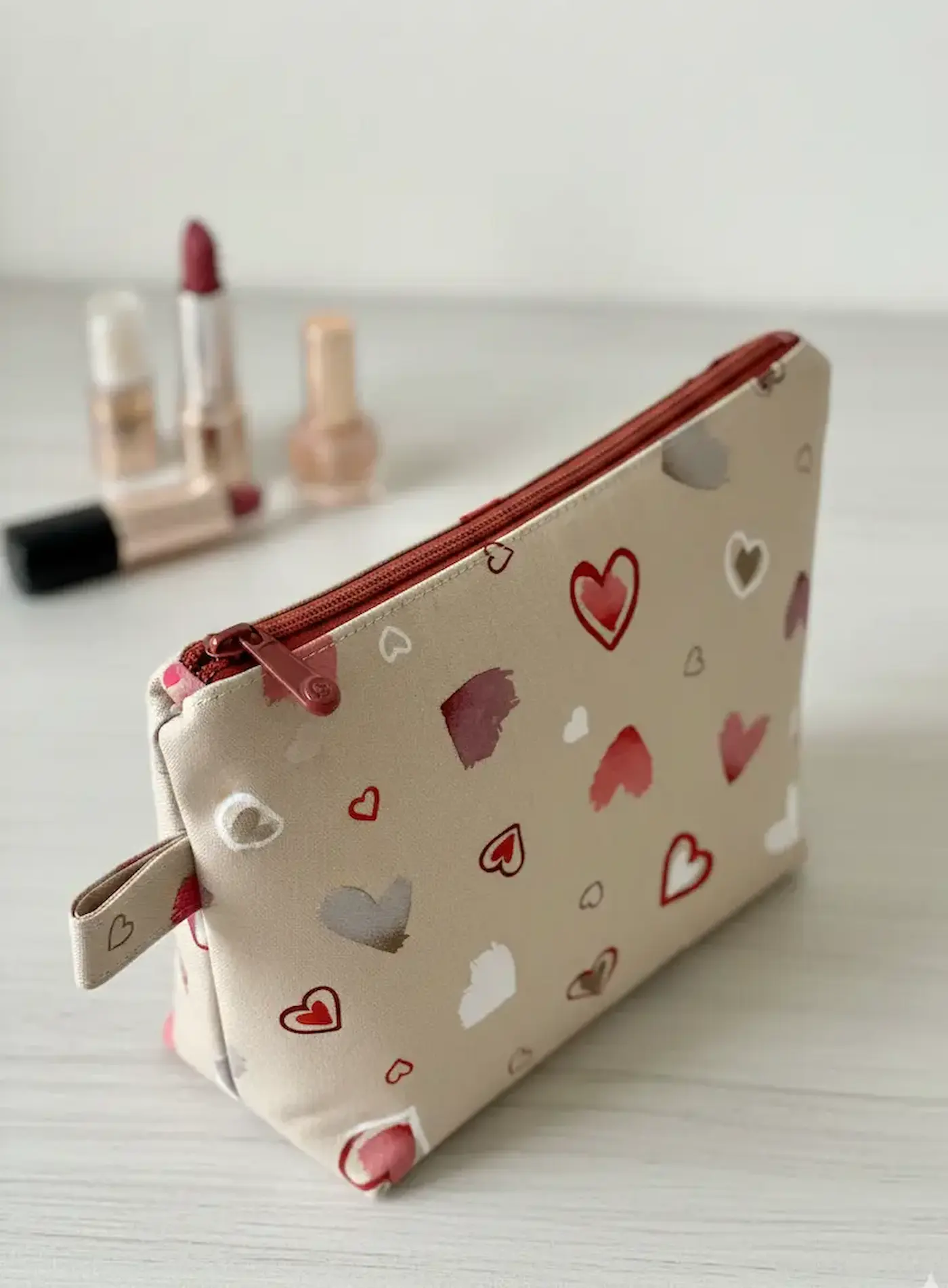 Handgenähte Kosmetiktasche aus robustem Dekostoff mit Herzmuster in Beige und Rot, stilvoll arrangiert mit Lippenstift.