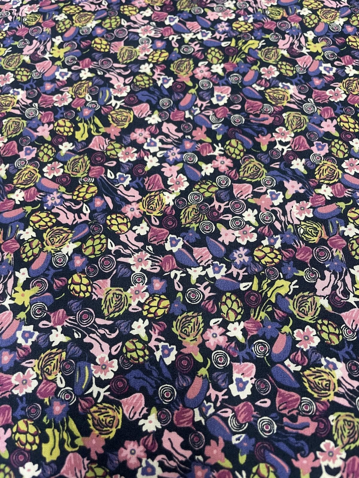 Detailaufnahme von Baumwoll-Popeline-Stoff als Meterware mit dichtem, floralem Allover-Muster in Lila, Rosa, Dunkelblau und Gelbgrün.