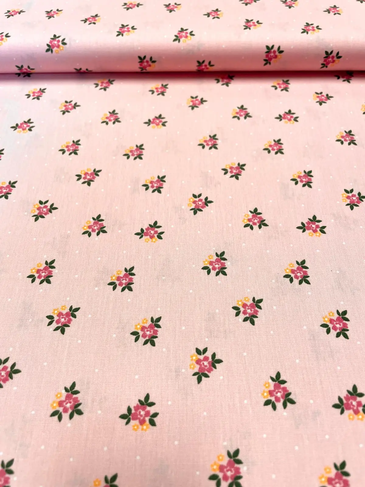 Zarter Baumwoll-Popeline-Stoff als Meterware in Hellrosa mit kleinen Streublumen und feinen weißen Punkten im Hintergrund.