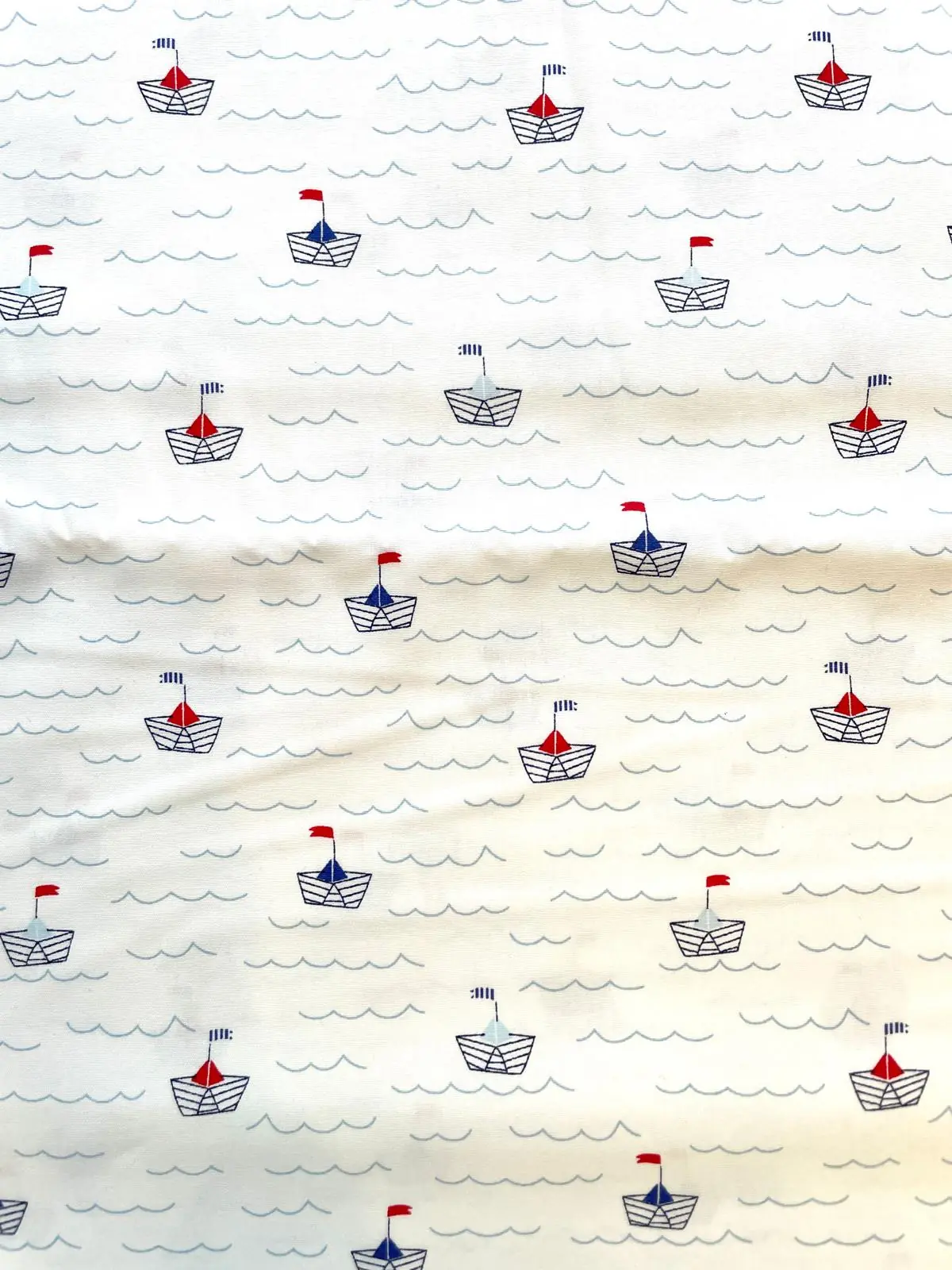 Makelloser, weißer Baumwoll-Popeline mit einem Rapport-Muster aus hellblauen Wellenlinien und kleinen blauen Papierbooten mit roten Segeln und gestreiften Flaggen.