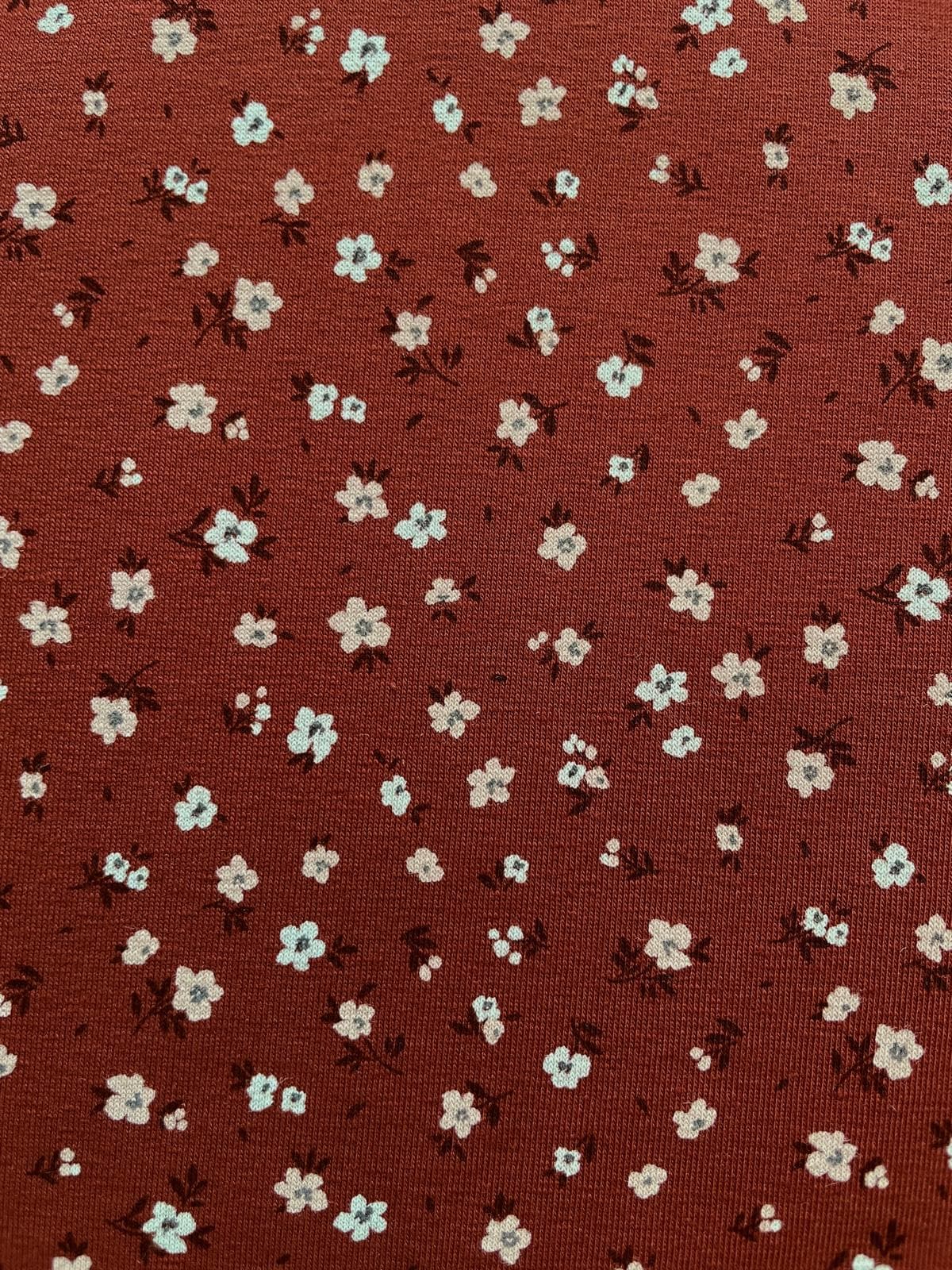 Weicher Jerseystoff in Rostbraun mit zierlichem weißen Blumenmuster, ideal für Kinderkleidung und Damenmode