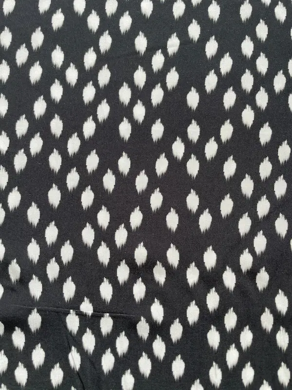 Hochwertiger Viskosestoff mit 15% Polyamid-Anteil. Das Muster zeigt weiß verschwommene Punkte im Ikat-Stil auf schwarzem Hintergrund. Der Stoff liegt flach und zeigt eine feine Gewebestruktur.