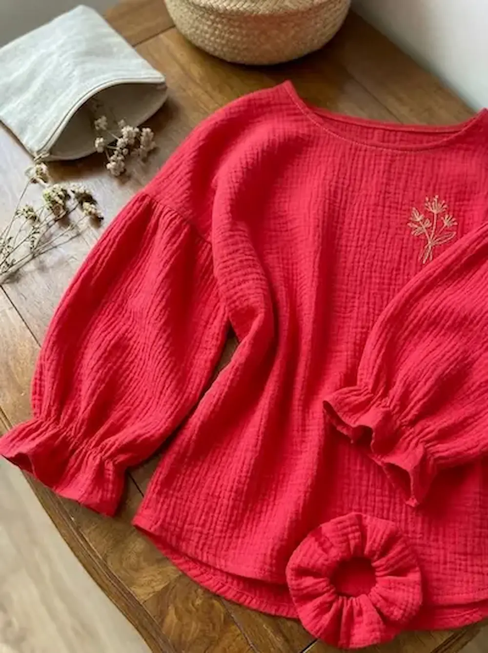 Rote Bio-Musselin Bluse mit Stickerei und passendem Haargummi (Scrunchie) auf einem Holztisch, nachhaltige Double Gauze Baumwoll-Meterware in kräftigem Rot.