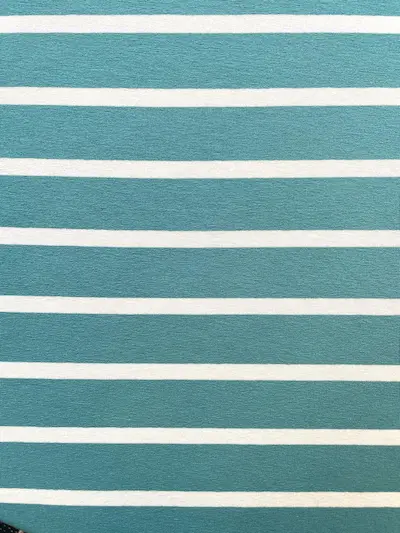 Detailansicht eines elastischen Viskosejersey-Stoffes mit horizontalen Streifen in Petrol und Weiß, feine Strickstruktur erkennbar.