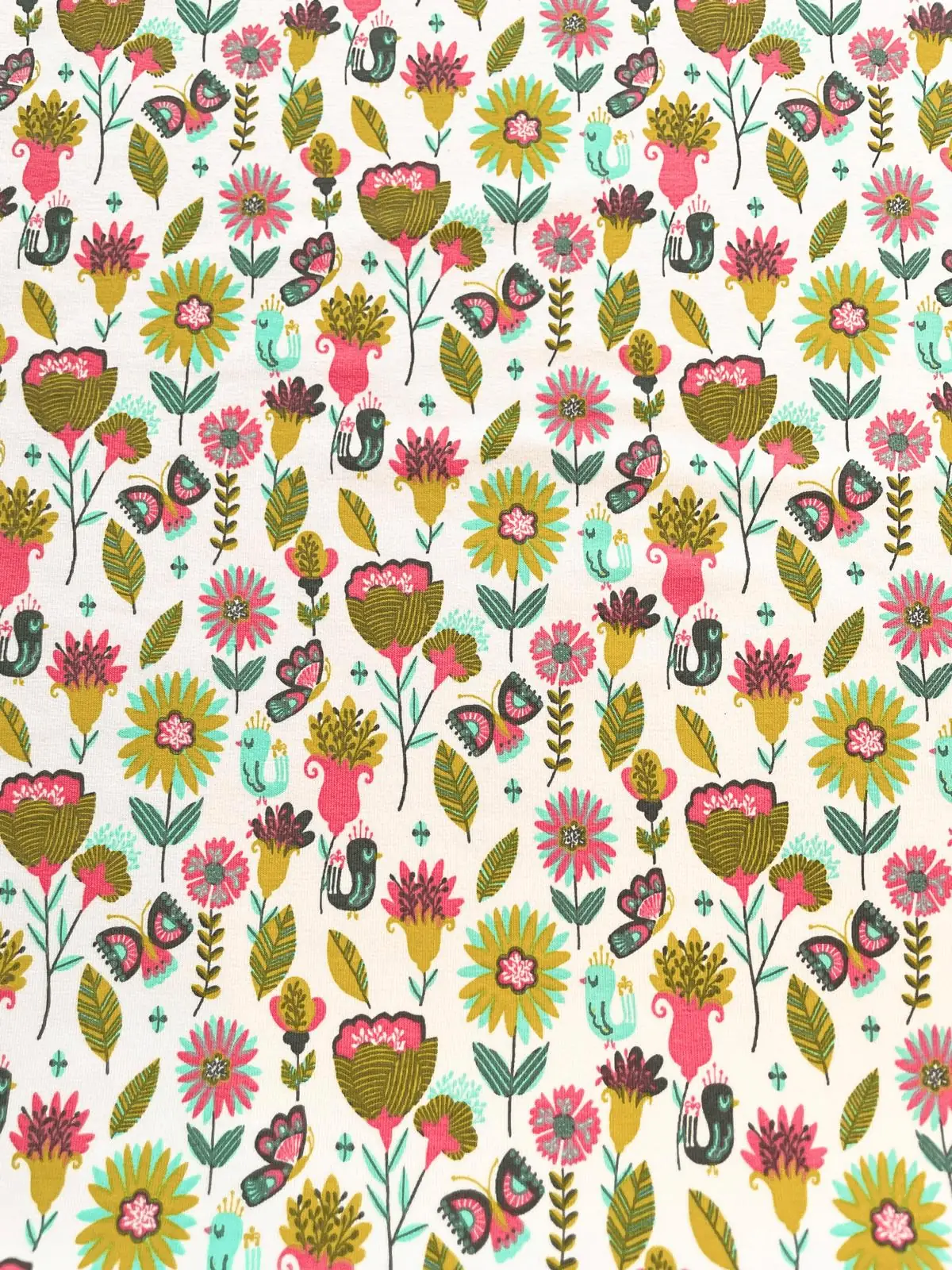 Nahaufnahme von angerautem Sweatstoff als Meterware mit einem dichten, bunten Allover-Print aus floralen Motiven, großen Blumen, Schmetterlingen und kleinen Vögeln in Pink, Senfgelb, Olivgrün und Türkis auf hellem Hintergrund.